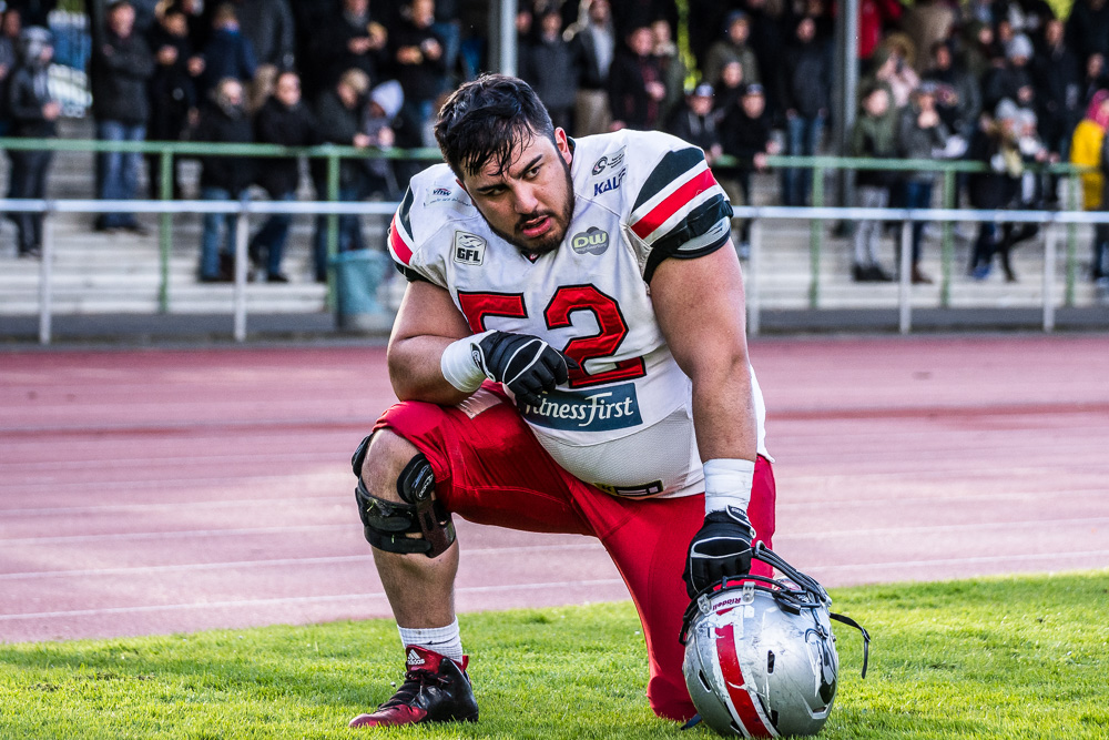 Sportfoto eines erschöpften, knieenden American Football Spielers am Spielfeldrand während eines Wettkampf